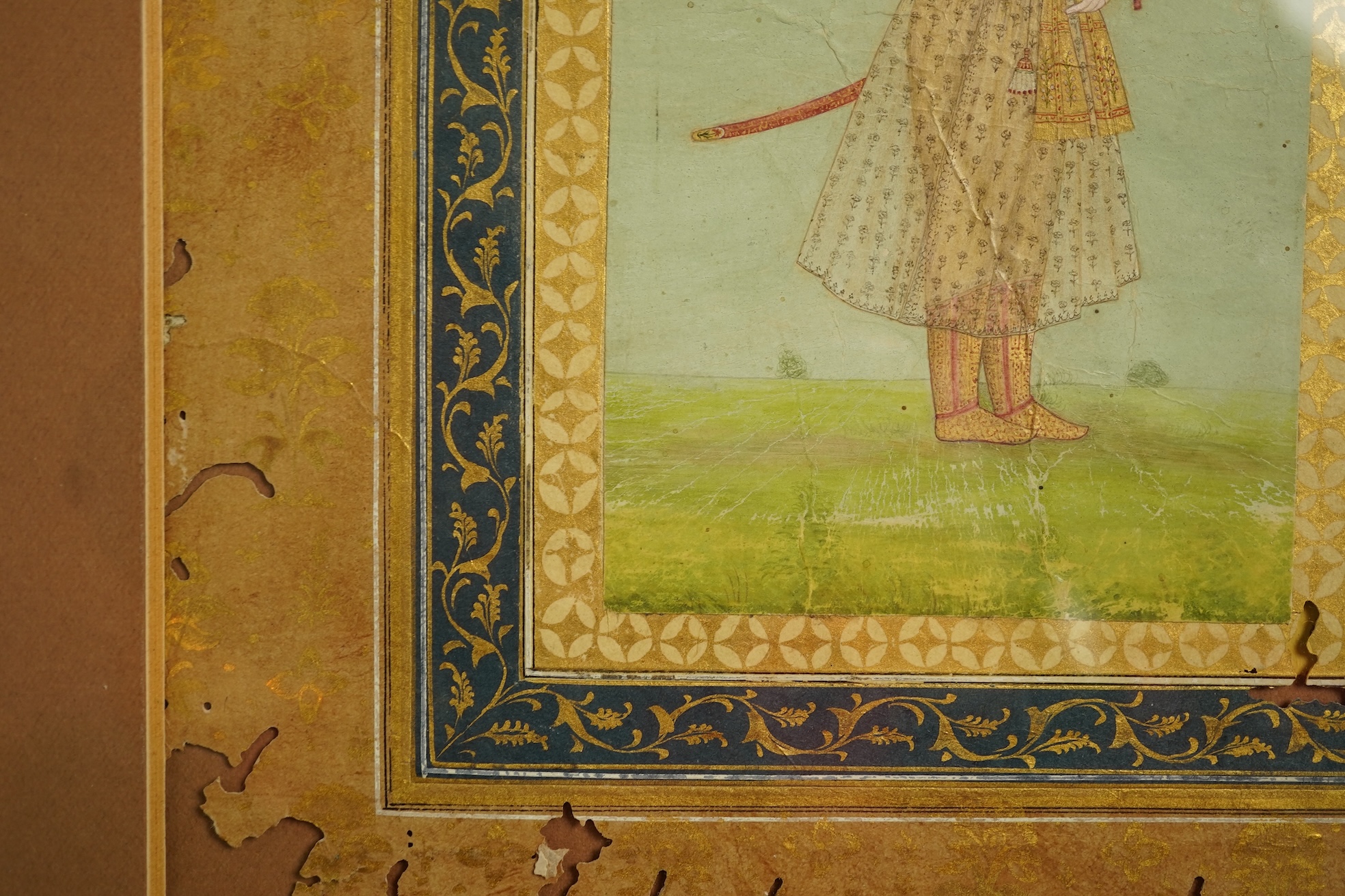 Mogul (Mughal) School , Profile Portrait of a Mogul dignitary, possibly Shah Jahan (1592-1666), full length, wearing court attire and a sword, standing in a landscape, watercolour miniature, 31cm x 20.5cm including borde